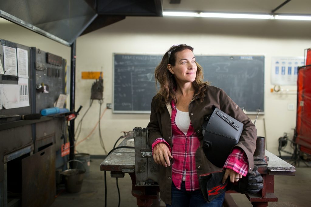 Female metal work teacher leaning against classroom workbench